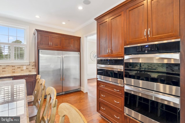 kitchen with backsplash, light wood-type flooring, light stone counters, stainless steel appliances, and ornamental molding