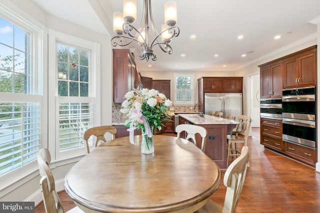 dining space with crown molding, an inviting chandelier, sink, and dark hardwood / wood-style floors