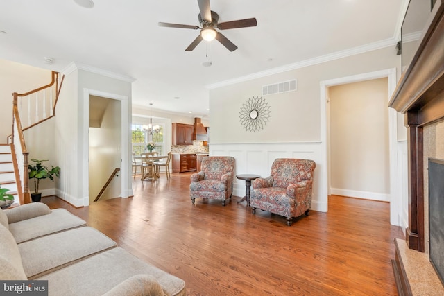 living room featuring crown molding, light hardwood / wood-style flooring, a high end fireplace, and ceiling fan with notable chandelier