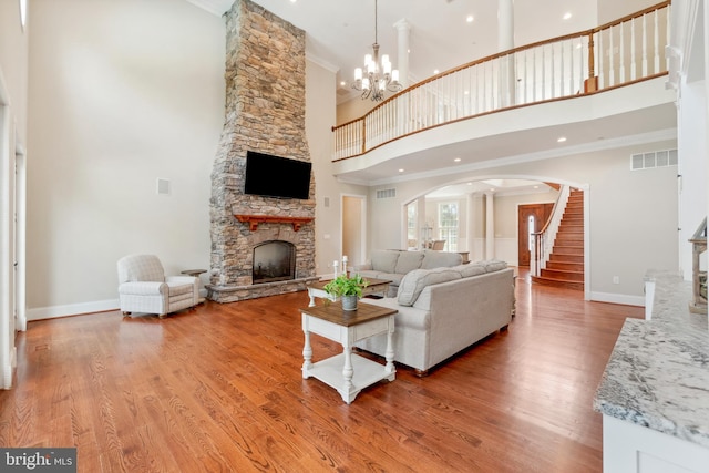 living room with crown molding, a chandelier, wood-type flooring, a stone fireplace, and a towering ceiling