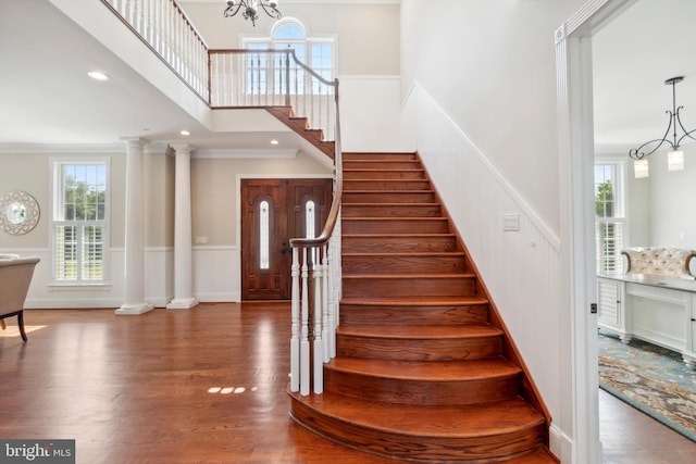 stairway featuring wood-type flooring, ornamental molding, a notable chandelier, and ornate columns