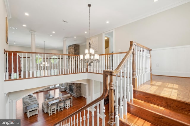 stairway with crown molding, hardwood / wood-style flooring, a chandelier, and ornate columns