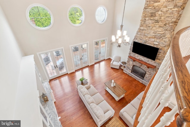 living room with a high ceiling, wood-type flooring, a notable chandelier, and a stone fireplace