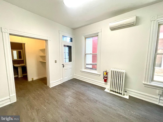 unfurnished bedroom featuring a wall mounted AC, multiple windows, dark hardwood / wood-style floors, and radiator heating unit