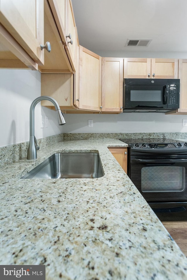 kitchen with sink, light stone counters, wood-type flooring, light brown cabinetry, and black appliances