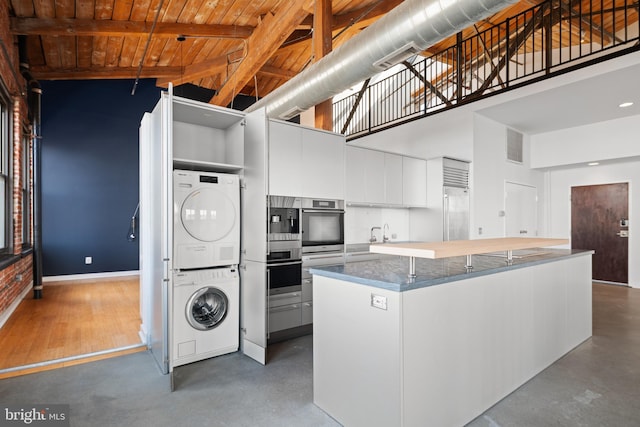 kitchen with wooden ceiling, stacked washer and clothes dryer, beamed ceiling, white cabinetry, and high vaulted ceiling