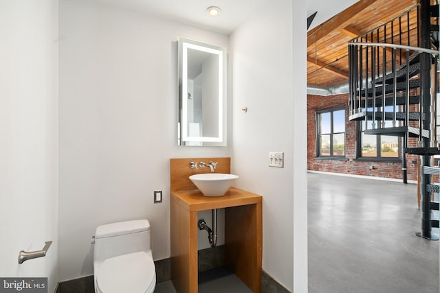 bathroom with brick wall, toilet, and sink