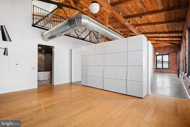 interior space with beamed ceiling, high vaulted ceiling, wooden ceiling, brick wall, and light hardwood / wood-style floors