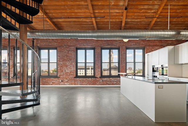 kitchen with oven, wood ceiling, white cabinetry, brick wall, and beam ceiling