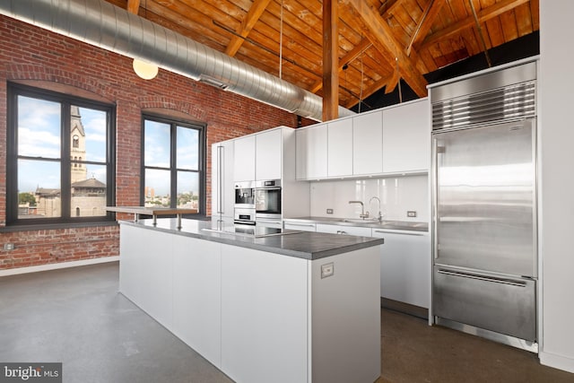 kitchen with brick wall, appliances with stainless steel finishes, a center island, white cabinetry, and vaulted ceiling with beams