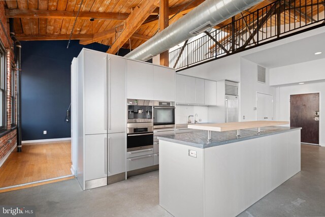 kitchen featuring a kitchen island, beam ceiling, wood ceiling, high vaulted ceiling, and white cabinetry