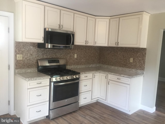 kitchen featuring dark wood-type flooring, baseboards, decorative backsplash, appliances with stainless steel finishes, and white cabinetry