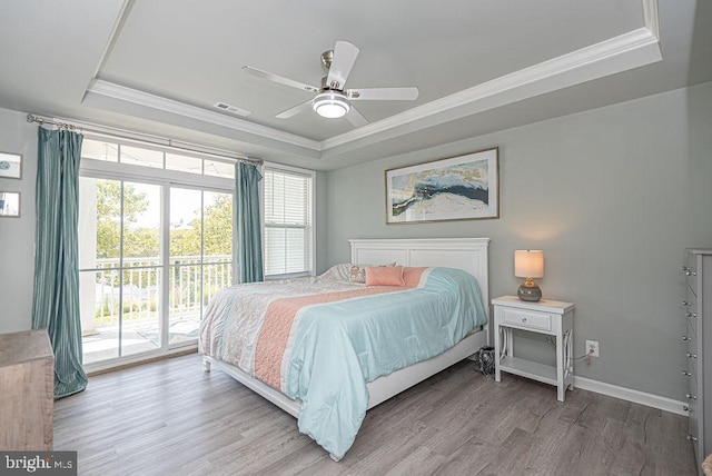 bedroom with a tray ceiling, access to exterior, wood-type flooring, and ceiling fan