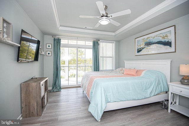 bedroom with a tray ceiling, crown molding, access to exterior, ceiling fan, and light wood-type flooring