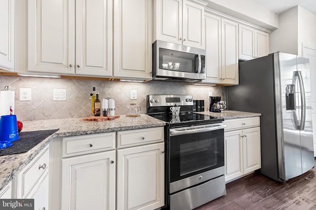 kitchen with light stone counters, decorative backsplash, appliances with stainless steel finishes, white cabinets, and dark wood-style flooring