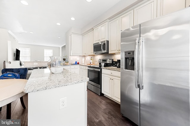 kitchen with light stone countertops, dark wood-type flooring, appliances with stainless steel finishes, white cabinetry, and tasteful backsplash