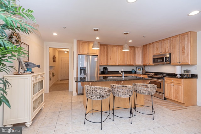 kitchen featuring light tile patterned floors, decorative light fixtures, stainless steel appliances, sink, and a center island with sink