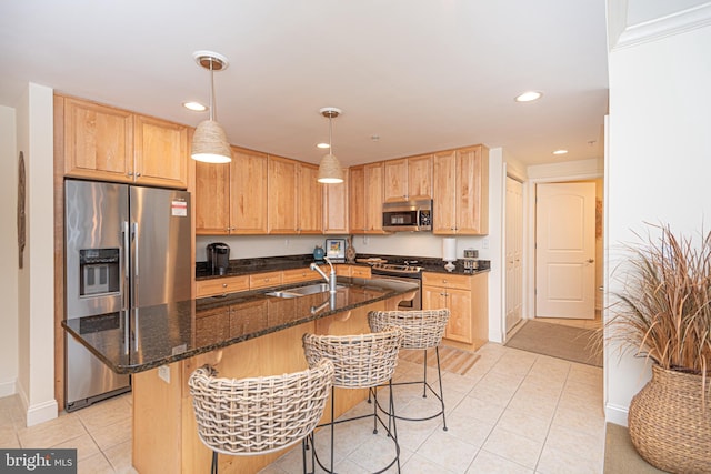 kitchen with an island with sink, hanging light fixtures, stainless steel appliances, sink, and dark stone countertops