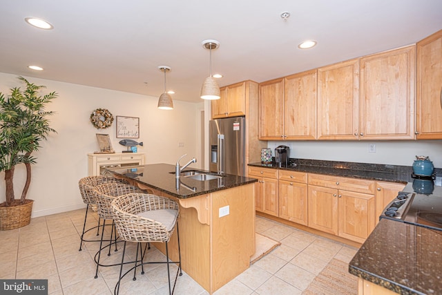 kitchen with dark stone countertops, light tile patterned floors, light brown cabinets, high end fridge, and a sink