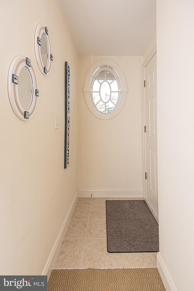 doorway with baseboards and tile patterned flooring