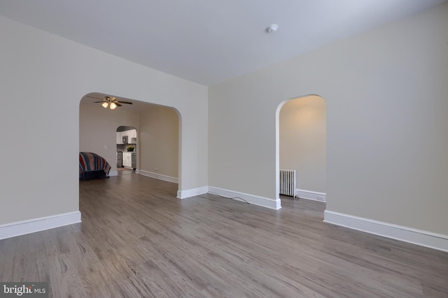 empty room with ceiling fan, radiator, and light wood-type flooring