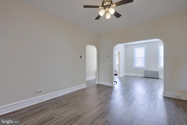 empty room with ceiling fan, dark hardwood / wood-style floors, and radiator heating unit