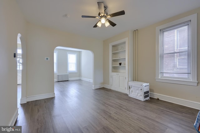 unfurnished living room featuring radiator heating unit, hardwood / wood-style flooring, built in shelves, and ceiling fan