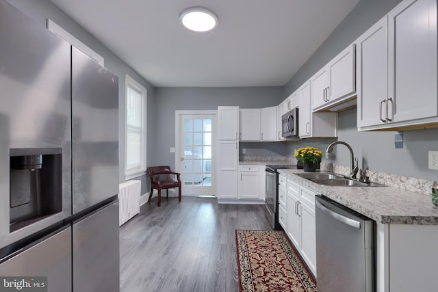 kitchen with light hardwood / wood-style floors, stainless steel appliances, sink, radiator heating unit, and white cabinets