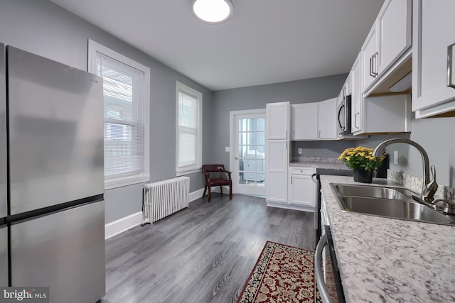 kitchen with radiator, stainless steel appliances, sink, hardwood / wood-style flooring, and white cabinets