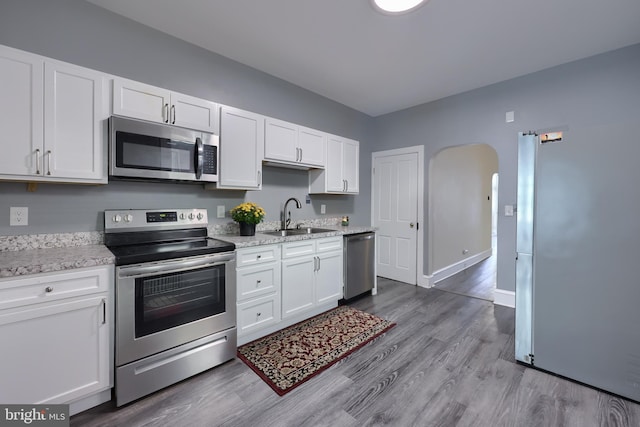 kitchen with stainless steel appliances, sink, hardwood / wood-style flooring, light stone counters, and white cabinets