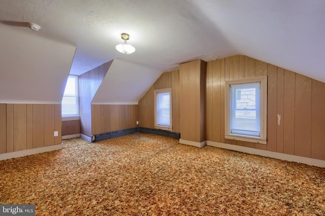 bonus room with a wealth of natural light, wooden walls, light carpet, and vaulted ceiling