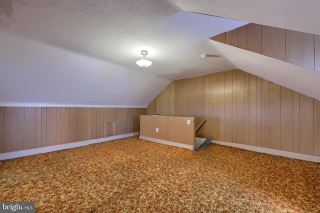 bonus room with lofted ceiling, wooden walls, carpet, and a textured ceiling