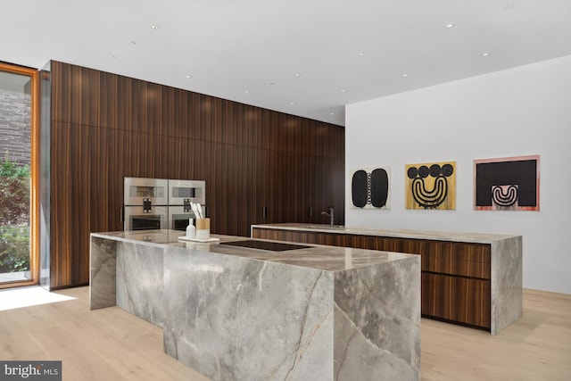 bar with sink, black electric cooktop, double oven, light stone countertops, and light hardwood / wood-style floors