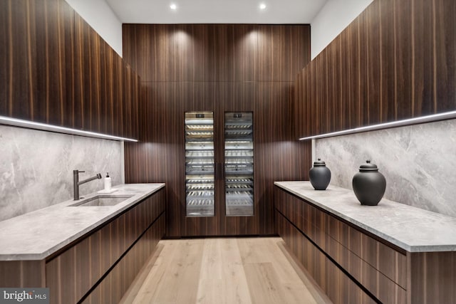 bar with dark brown cabinets, light wood-type flooring, decorative backsplash, and sink