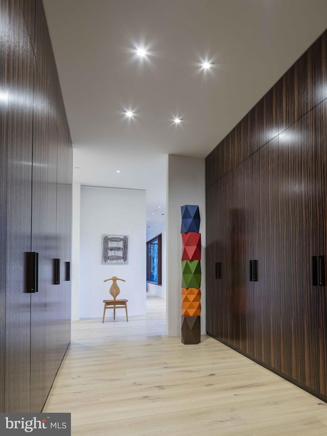 hallway with light wood-type flooring and wooden walls