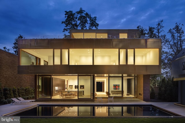 back house at night featuring a balcony and a patio