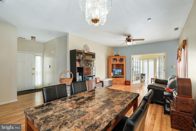 dining space with ceiling fan with notable chandelier, french doors, and light hardwood / wood-style flooring