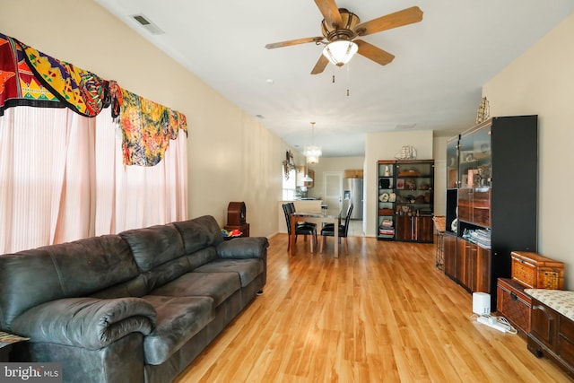 living room with ceiling fan with notable chandelier and light hardwood / wood-style flooring