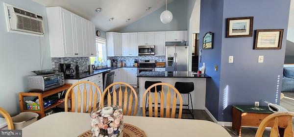 kitchen featuring white cabinets, hanging light fixtures, backsplash, high vaulted ceiling, and appliances with stainless steel finishes