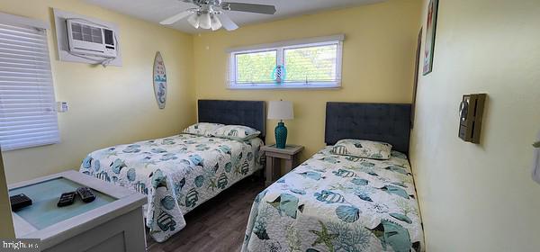 bedroom with a wall mounted AC, dark hardwood / wood-style floors, and ceiling fan