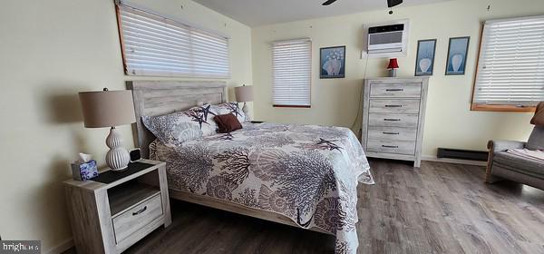 bedroom with multiple windows, ceiling fan, a wall mounted air conditioner, and hardwood / wood-style flooring