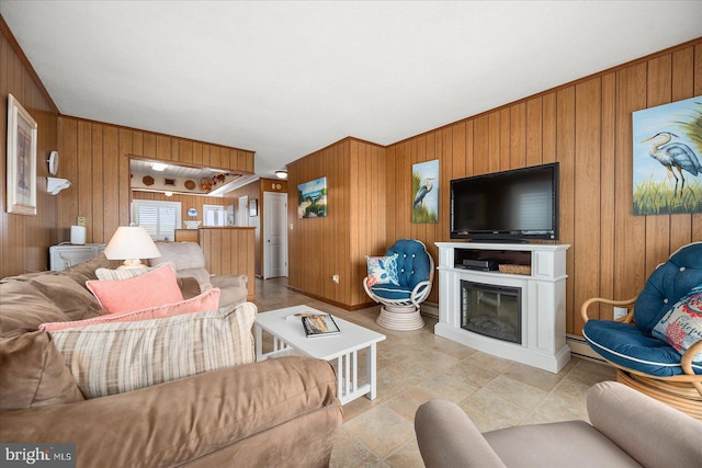 living area featuring wood walls, a baseboard heating unit, and a glass covered fireplace