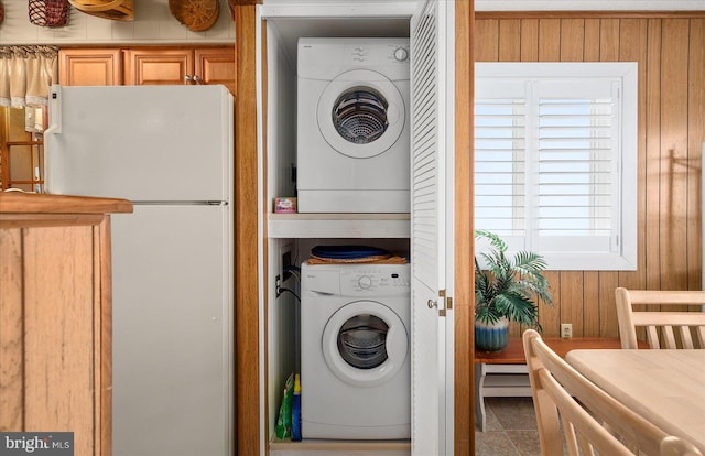 clothes washing area featuring stacked washer and dryer, laundry area, baseboard heating, and wood walls