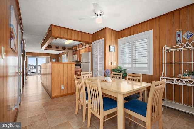 dining room with ceiling fan and wooden walls