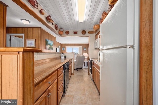 kitchen with white appliances, wooden walls, light countertops, and brown cabinetry