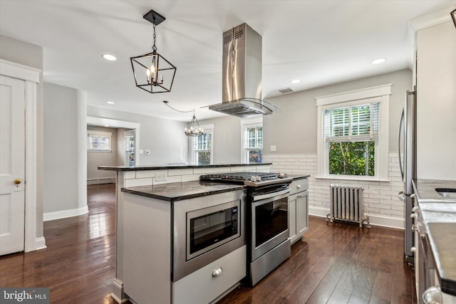 kitchen featuring island range hood, dark hardwood / wood-style floors, decorative light fixtures, appliances with stainless steel finishes, and radiator heating unit