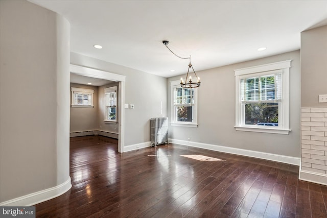 unfurnished dining area with dark hardwood / wood-style flooring, a baseboard heating unit, an inviting chandelier, and radiator