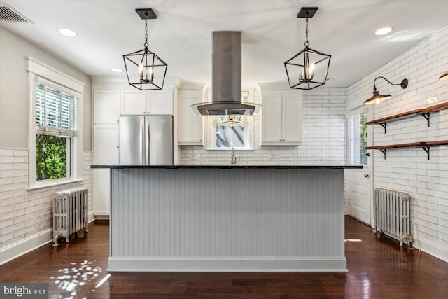 kitchen featuring island exhaust hood, radiator heating unit, white cabinets, and stainless steel refrigerator