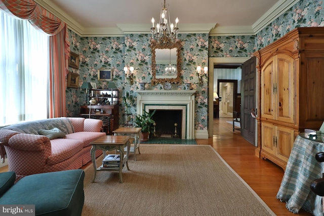 living area with a chandelier, a fireplace with flush hearth, wallpapered walls, and crown molding