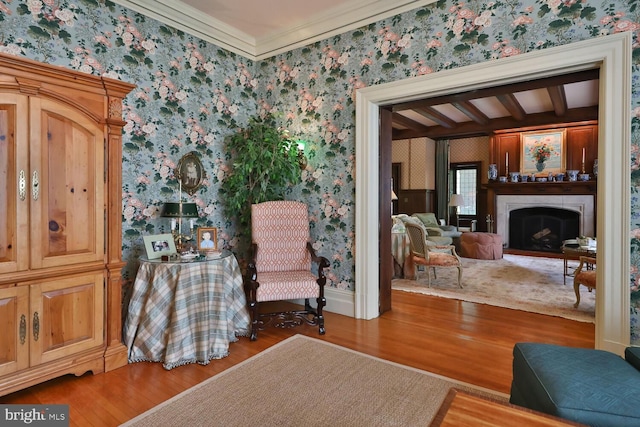 living area featuring beam ceiling, a fireplace, wallpapered walls, and wood finished floors